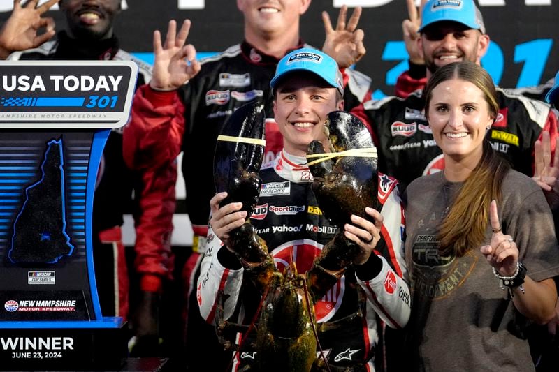 Christopher Bell, front left, holds up a lobster while standing with his wife Morgan, front right, as they celebrate after he won the NASCAR Cup Series race at New Hampshire Motor Speedway, Sunday, June 23, 2024, in Loudon, N.H. (AP Photo/Steven Senne)