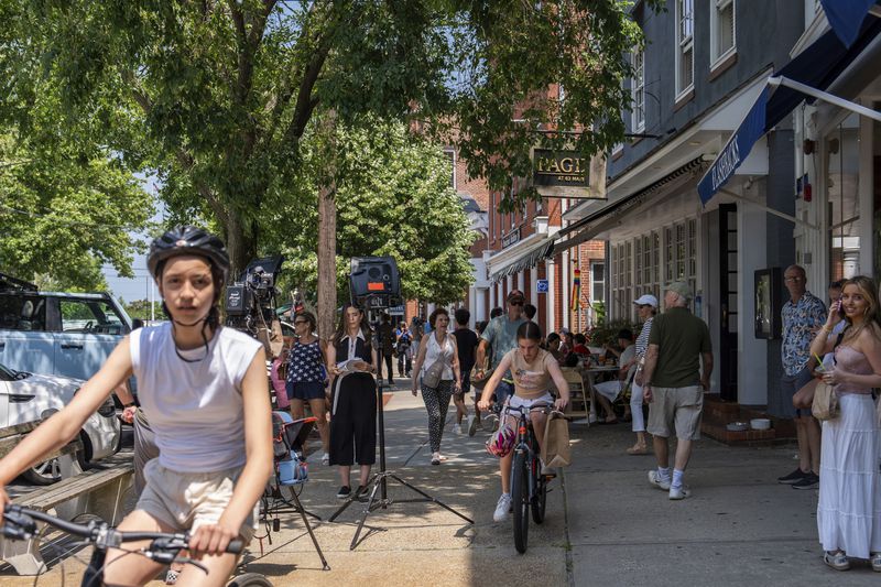 People walk and ride bikes along Main Street as a reporter does a stand up, Tuesday, June 18, 2024, in Sag Harbor, N.Y. (AP Photo/Julia Nikhinson)