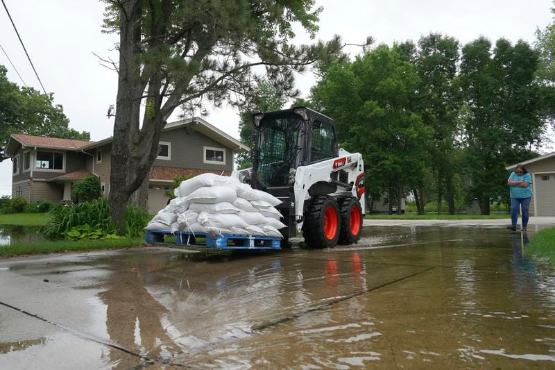 Water surrounds Tim and Sarah Smith's home while he uses a Bobcat to move a pallet of sandbags as heavy rains have caused both Tetonka Lake and Sakatah Lake to rise threatening to flood nearby homes and businesses Thursday, June 20, 2024, in Waterville, Minn. (Anthony Souffle/Star Tribune via AP)