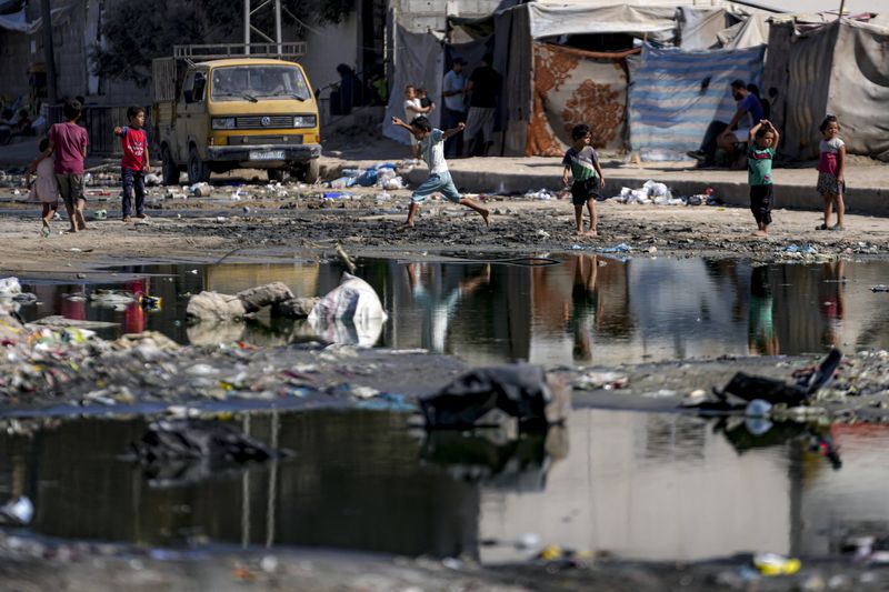 Displaced children walk through a dark streak of sewage flowing into the streets of Deir al-Balah, central Gaza Strip, Thursday, Aug. 29, 2024. (AP Photo/Abdel Kareem Hana)