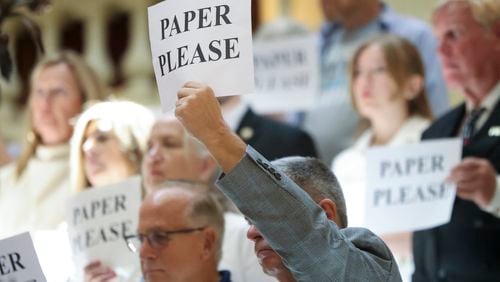 A protester holds a “Paper Please” sign during a press conference Monday at the Georgia Capitol in support of paper ballots. (Jason Getz / AJC)