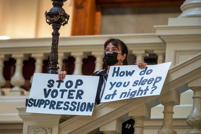 Ann White of Roswell holds signs to protest against an overhaul of the state's election laws on Thursday as she stands on the North Wing stairs of the Georgia Capitol. The House and Senate on Thursday both passed the measure, Senate Bill 202. Gov. Brian Kemp then signed it into law. “It ain’t over yet,” White said. “I look forward to going door to door working against everybody that voted for (SB 202).” (Alyssa Pointer / Alyssa.Pointer@ajc.com)