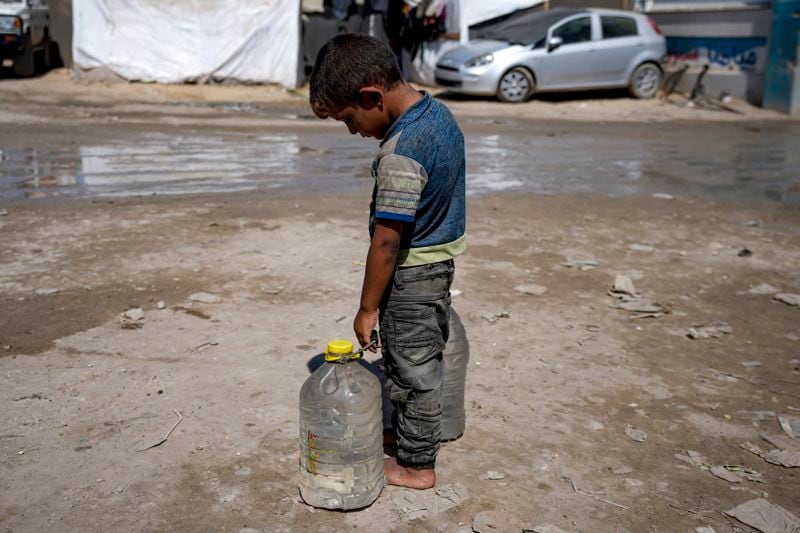 A displaced child carries filled water bottles at a makeshift tent camp in Deir al-Balah, central Gaza Strip, Thursday, Aug. 29, 2024. (AP Photo/Abdel Kareem Hana)