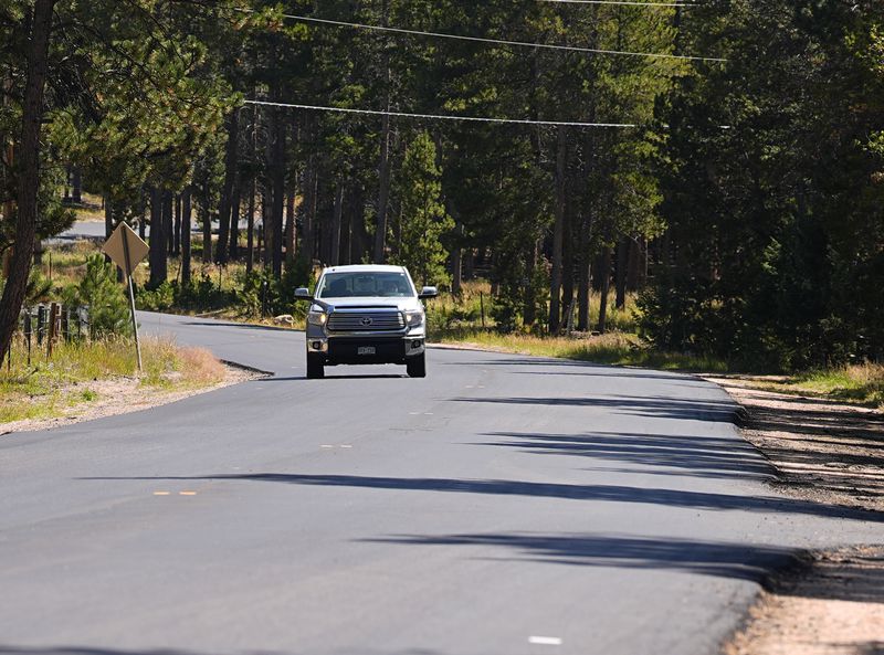 A motorist guides a pickup truck along the 23000 block of Pleasant Park Road where a teenager, who was scouting for a location for lakeside homecoming photos, was shot in the face by a town councilman, Friday, Sept. 13, 2024, near Conifer, Colo. (AP Photo/David Zalubowski)