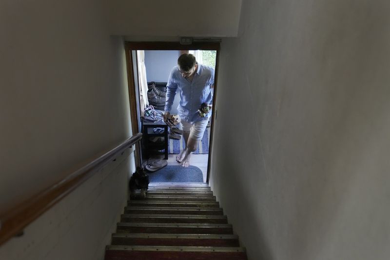 Steven Manetta, a cancer patient, returns from the garden with an eggplant for dinner as his dog Basil leads him up the stairs Thursday, Aug. 29, 2024, in his Lemont, Ill., home. (AP Photo/Charles Rex Arbogast)