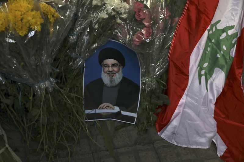 A poster of Hezbollah leader Sayyed Hassan Nasrallah is placed next to bouquets of flowers and Lebanese flag in front of the Lebanese Embassy in Tehran, Iran, Wednesday, Sept. 18, 2024. (AP Photo/Vahid Salemi)