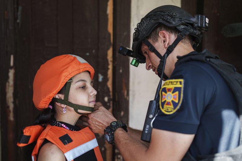 A Fenix team rescue worker places a helmet on a girl during the evacuation of local population to safe areas, in Selidove, Donetsk region, Ukraine, on Tuesday, August 20, 2024. (AP Photo/Evgeniy Maloletka)