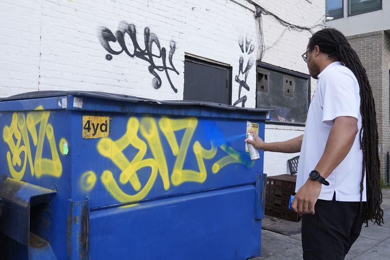 Aceba Broadus paints over graffiti in a neighborhood of Washington, Tuesday, Aug. 20, 2024. (AP Photo/Susan Walsh)