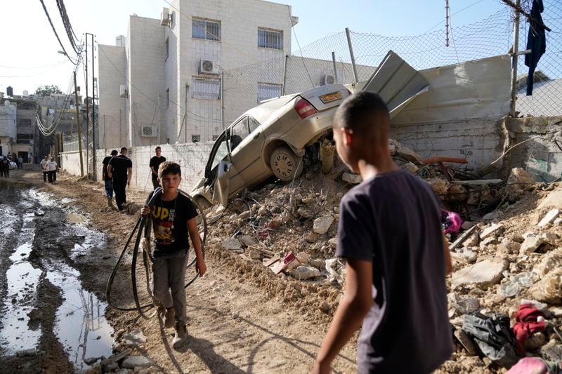 Palestinian refugees walk past a damaged vehicle in the West Bank refugee camp of Tulkarem, Thursday, Sept. 12, 2024. (AP Photo/Nasser Nasser)