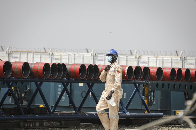 FILE - A Ugandan worker from China Oilfield Services Limited (COSL), a contractor for China National Offshore Oil Corporation (CNOOC), walks near pipes at the Kingfisher oil field on the shores of Lake Albert in the Kikuube district of western Uganda Tuesday, Jan. 24, 2023. (AP Photo/Hajarah Nalwadda, File)