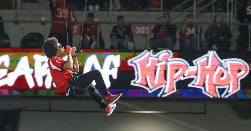 Ludacris descends from the top of the stadium while performing during the game.  The Atlanta Falcons celebrate Hip-Hop 50 with performances and appearances during their NFL football game between the Atlanta Falcons and the New Orleans Saints in Atlanta on Sunday, Nov. 26, 2023.   (Bob Andres for the Atlanta Journal Constitution)