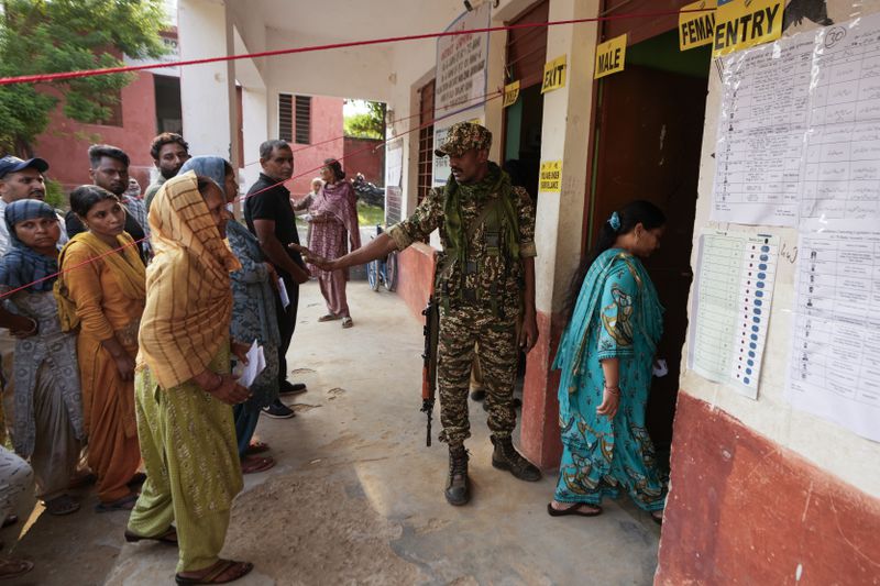 A paramilitary soldier guards as people queue up to cast their vote at a polling booth during the final phase of an election to choose a local government in Indian-controlled Kashmir, in Jammu, India, Tuesday, Oct.1, 2024. (AP Photos/Channi Anand)