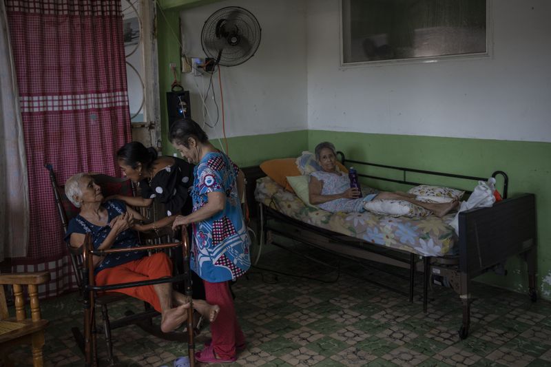 Maria Tiburcio, 77, back, rests in her bed under a fan at the Cogra nursing home, as director Maria Teresa Mendoza greets a patient, in Veracruz, Mexico, Sunday, June 16, 2024. Victims in Veracruz have made up nearly a third of Mexico's heat-related deaths as temperatures have reached 100 degrees in the humid Mexican gulf state. (AP Photo/Felix Marquez)