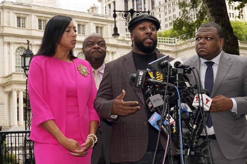 Shamel Kelly, center, flanked by his attorneys Bernarda Villalona, left, and Harry Daniels, right, speaks during a news conference in New York's City Hall Park, Tuesday, Oct. 1, 2024. (AP Photo/Richard Drew)