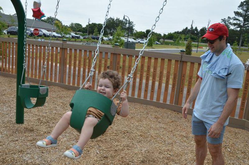 Jordan Johnson plays with his 18-month-old son, Micah, at the opening of the new PlayTown Suwanee playground. Johnson grew up playing on the original PlayTown Suwanee. (Photo Courtesy of Curt Yeomans)