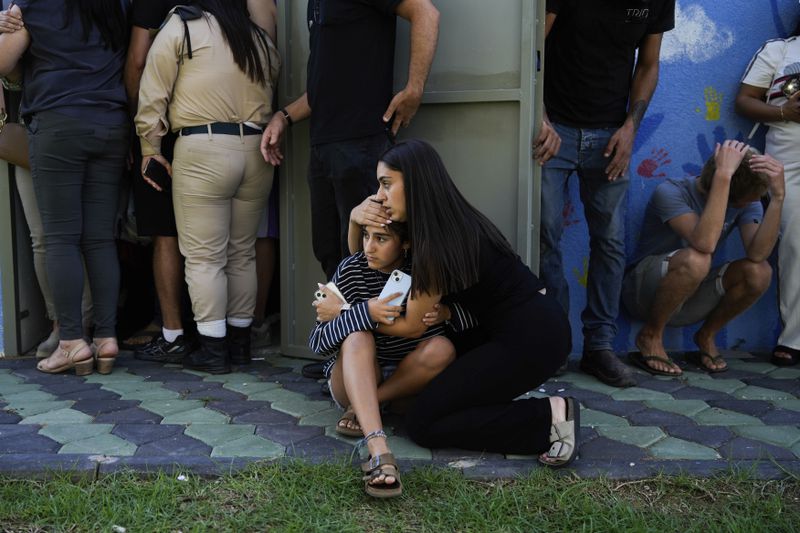 Israelis take cover next to a shelter as a siren sounds a warning of incoming rockets fired from Lebanon, in Nahariya, northern Israel, Thursday, Sept. 19, 2024. (AP Photo/Baz Ratner)