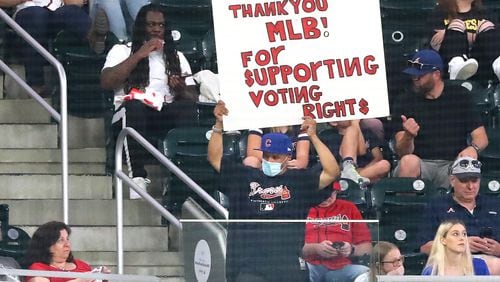 A fan - wearing a Braves jersey and a Cubs hat - holds a sign thanking Major League Baseball for "supporting voting rights" during the fifth inning of a Braves-Cubs game Monday, April 26, 2021, at Truist Park in Atlanta.  MLB moved the 2021 All-Star Game out of Atlanta over Georgia's new voting law. The July 13 game will now be played in Denver. (Curtis Compton / Curtis.Compton@ajc.com)