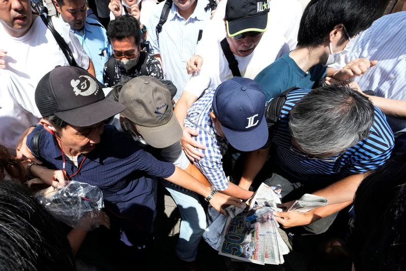 Pedestrians try to obtain an extra edition of the Sports Hochi newspaper reporting on the Los Angeles Dodgers' Shohei Ohtani becoming the first player in major league history with 50 home runs and 50 stolen bases in a season, Friday, Sept. 20, 2024, in Tokyo. (AP Photo/Eugene Hoshiko)