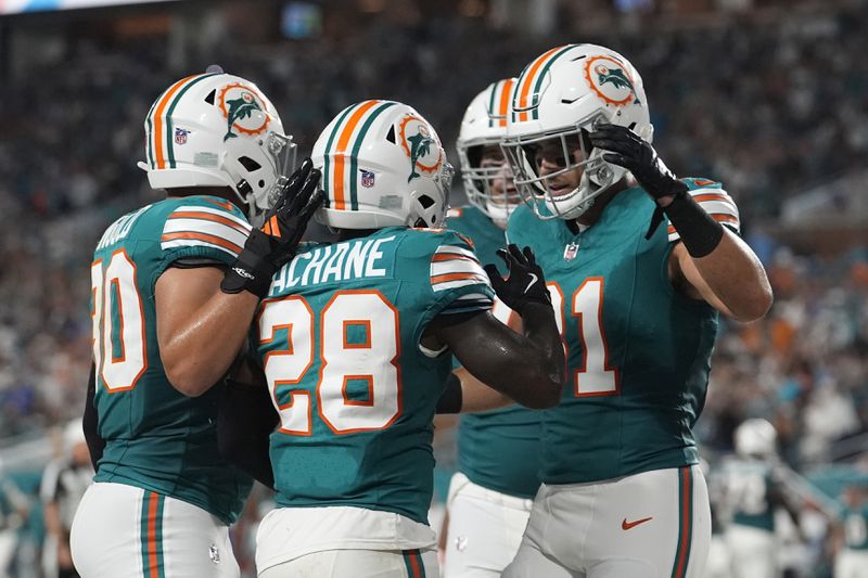 Miami Dolphins running back De'Von Achane (28) is congratulated by his teammates after scoring a touchdown during the first half of an NFL football game against the Buffalo Bills, Thursday, Sept. 12, 2024, in Miami Gardens, Fla. (AP Photo/Lynne Sladky)