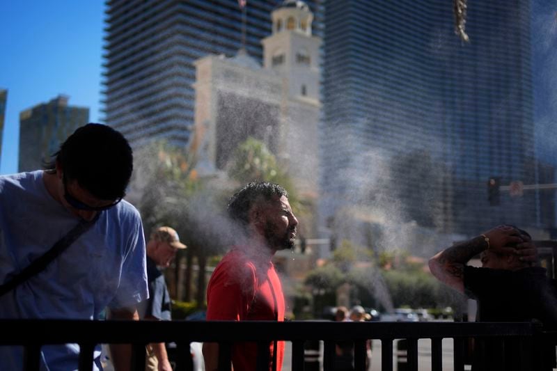 People cool off in misters along the Las Vegas Strip, Sunday, July 7, 2024, in Las Vegas. A heat wave is spreading across the Western U.S., the National Weather Service said, sending many residents in search of a cool haven from the dangerously high temperatures. (AP Photo/John Locher)