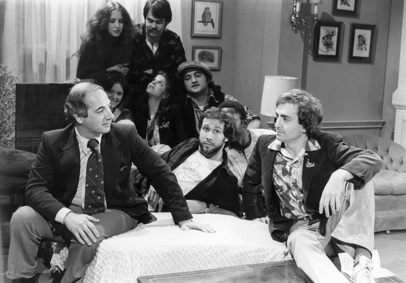 FILE - White House Press Secretary Ron Nessen, left, appears on the "Saturday Night Live" set with producer Lorne Michaels, right, and cast members Chevy Chase, foreground center, Laraine Newman, background left, Dan Aykroyd, background right, Jane Curtain, second row from left, Gilda Radner, John Belushi and Garret Morris, partially obscured, on April 17, 1976, in New York. (AP Photo)