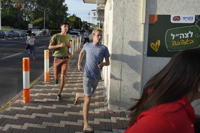 Israelis run to take cover as a siren sounds a warning of incoming rockets fired from Lebanon, in Nahariya, northern Israel, Thursday, Sept. 19, 2024. (AP Photo/Baz Ratner)