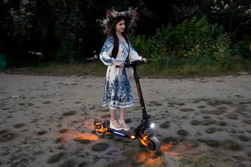 A festively dressed Ukrainian woman rides a scooter in a modern take of a traditional Ukrainian celebration of Kupala Night, in Warsaw, Poland, on Saturday, June 22, 2024. Ukrainians in Warsaw jumped over a bonfire and floated braids to honor the vital powers of water and fire on the Vistula River bank Saturday night, as they celebrated their solstice tradition of Ivan Kupalo Night away from war-torn home. (AP Photo/Czarek Sokolowski)