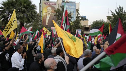 Iranian protesters wave Iranian, Palestinian and Lebanon's militant Hezbollah group flags in a demonstration to condemn the killing of Hamas leader Ismail Haniyeh as a huge portrait of him is seen on a wall at background, at Felestin (Palestine) Sq. in Tehran, Iran, Wednesday, July 31, 2024. Two back-to-back strikes in Beirut and Tehran, both attributed to Israel and targeting high-ranking figures in Hezbollah and Hamas, have left Hezbollah and Iran in a quandary. (AP Photo/Vahid Salemi)