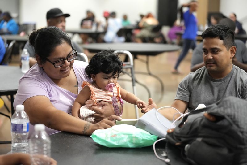 Keyla Herrera entertains her eight-month-old daughter, Emma, with a movie on her cell phone next to her husband, Edgar, as they sat inside of the cooling center set up inside of Sunnyside Health and Multi-Service Center on Wednesday, July 10, 2024, after Hurricane Beryl hit the Houston area on Monday. (Karen Warren/Houston Chronicle via AP)