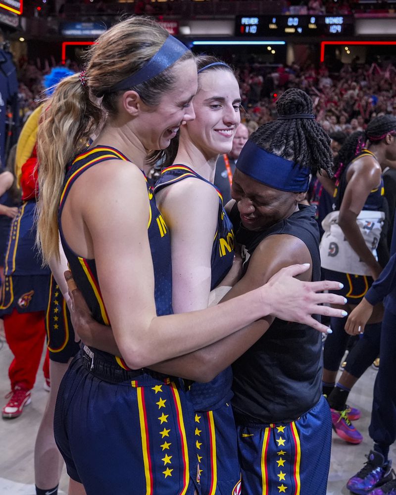 Indiana Fever guard Caitlin Clark, center is hugged by Lexie Hull, left, and Erica Wheeler (17) after a WNBA basketball game against the Dallas Wings in Indianapolis, Sunday, Sept. 15, 2024. (AP Photo/Michael Conroy)