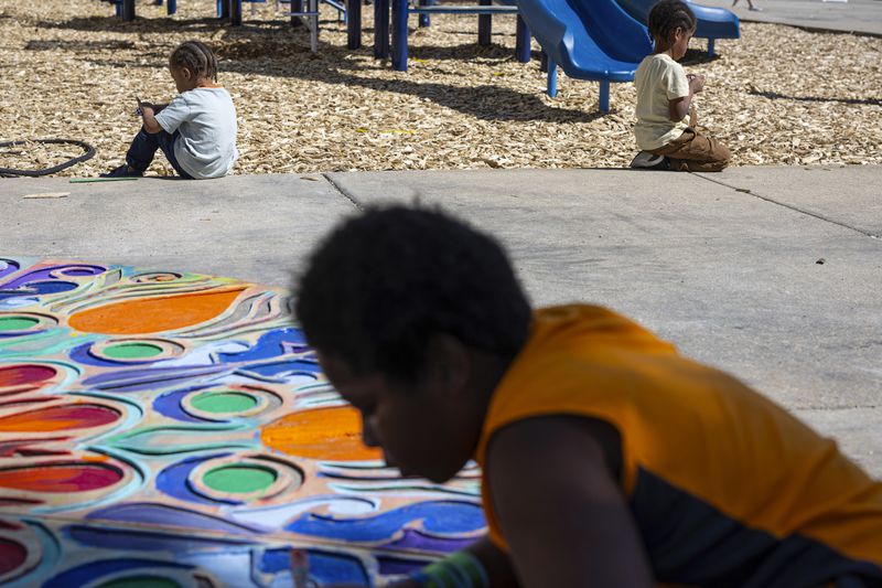 A child helps paint a display on the ground at a back to school health fair in Milwaukee, on Saturday Aug. 10, 2024. (AP Photo/Jeffrey Phelps)