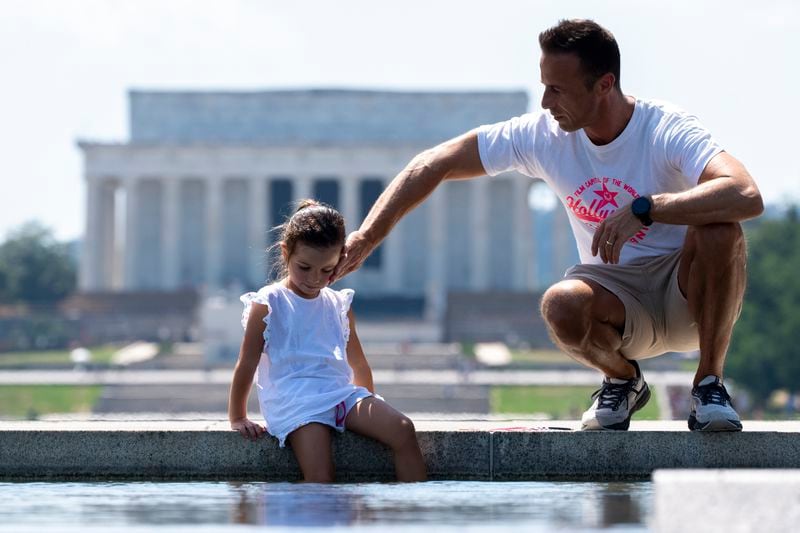 Andrea Di Miele, right, from Hoboken, N.J., puts water on his daughter, Sofia Di Miele, 10, with the Lincoln Memorial behind, near the World War II Memorial, Friday, June 21, 2024, in Washington. Temperatures are forecast to reach 100 degrees on Saturday. (AP Photo/Alex Brandon)