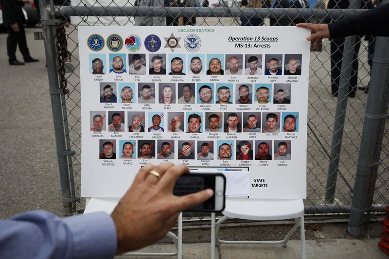 A reporter uses his telephone to photograph a poster showing suspected members of MS-13 in Los Angeles in 2017. ASSOCIATED PRESS