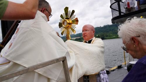 Bishop Edward Lohse, apostolic administrator of the Catholic Diocese of Steubenville, left, hands the Eucharist to the Rev. Roger Landry as they board a boat on the Ohio River as part of the National Eucharistic Pilgrimage, at the Steubenville Marina in Steubenville, Ohio, Sunday, June 23, 2024. (AP Photo/Jessie Wardarski)