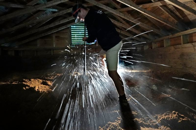 Ice chips fly as Nate Lord chops out a block at Rockywold Deephaven Camps, Thursday, June 20, 2024, in Holderness, N.H. Ice harvested from Squam Lake during the winter is insulated with sawdust in an ice house. It is used for refrigeration in ice boxes at each guest cabin throughout the summer. (AP Photo/Robert F. Bukaty)