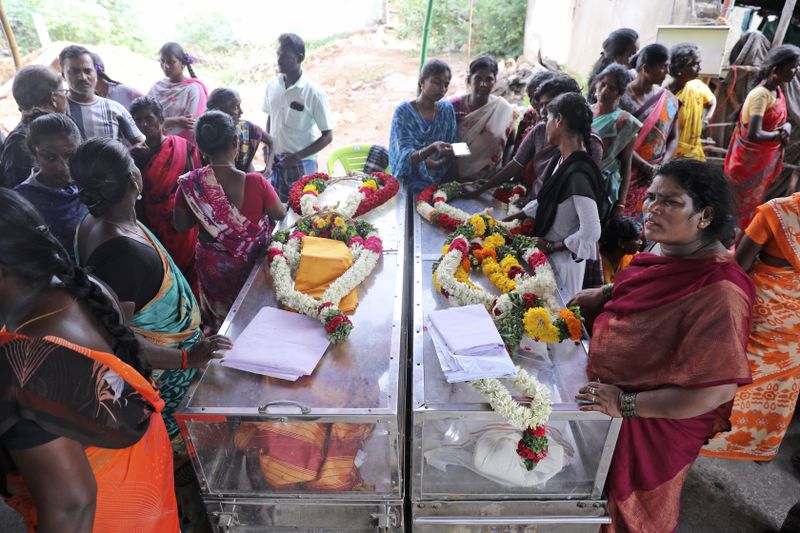 Relatives of a married couple, who died after drinking illegally brewed liquor, stand next to the caskets containing their bodies, in Kallakurichi district of the southern Indian state of Tamil Nadu, India, Thursday, June 20, 2024. The state's chief minister M K Stalin said the 34 died after consuming liquor that was tainted with methanol, according to the Press Trust of India news agency. (AP Photo/R. Parthibhan)