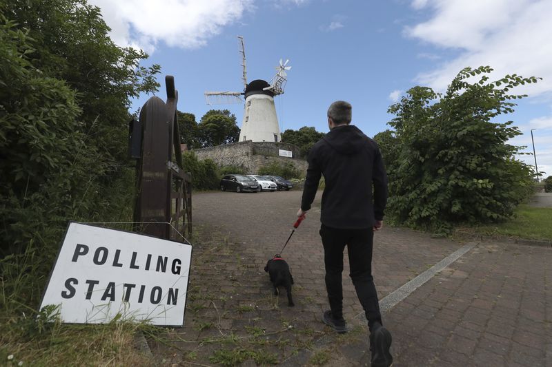 A man and his dog walk towards Falwell windmill and mill which is a temporary polling station in Sunderland, England, Thursday, July 4, 2024.Britain goes to the polls Thursday after Prime Minister Rishi Sunak called a general election. (AP Photo/Scott Heppell)