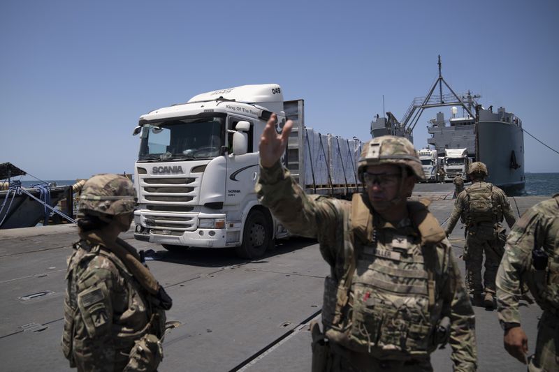 A U.S. Army soldier gestures as trucks loaded with humanitarian aid arrive at the U.S.-built floating pier Trident before reaching the beach on the coast of the Gaza Strip, Tuesday, June 25, 2024. (AP Photo/Leo Correa)
