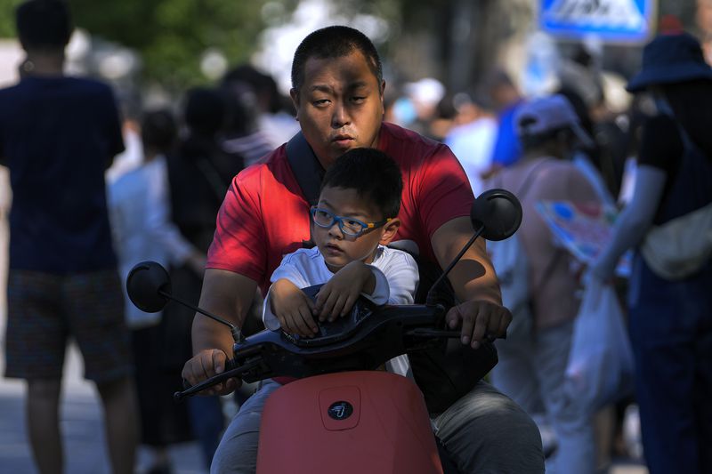 A man uses an electric bike to pick up his child after school in Beijing, Friday, Sept. 13, 2024. (AP Photo/Andy Wong)