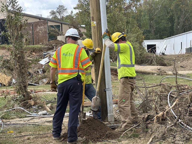 Contractors for Duke Energy dig a hole by hand to replace a utility pole in an area of destroyed electrical lines near the Swannanoa River in Asheville, N.C., on Friday, Oct. 4, 2024. (AP Photo/Jeff Amy)