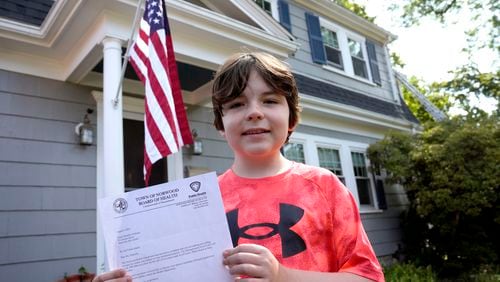 Danny Doherty, 12, of Norwood, Mass., stands for a photograph Wednesday, Aug. 21, 2024, in front of his home in Norwood, while holding a letter from the Town of Norwood Board of Health advising his family that they may not sell homemade ice cream at an ice cream stand near their home. (AP Photo/Steven Senne)