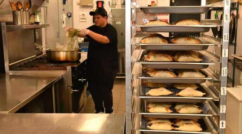 Freshly baked empanadas cool while filling ingredients cook in the background of the kitchen at Belén de la Cruz Empanadas & Pastries. (Chris Hunt for The Atlanta Journal-Constitution)
