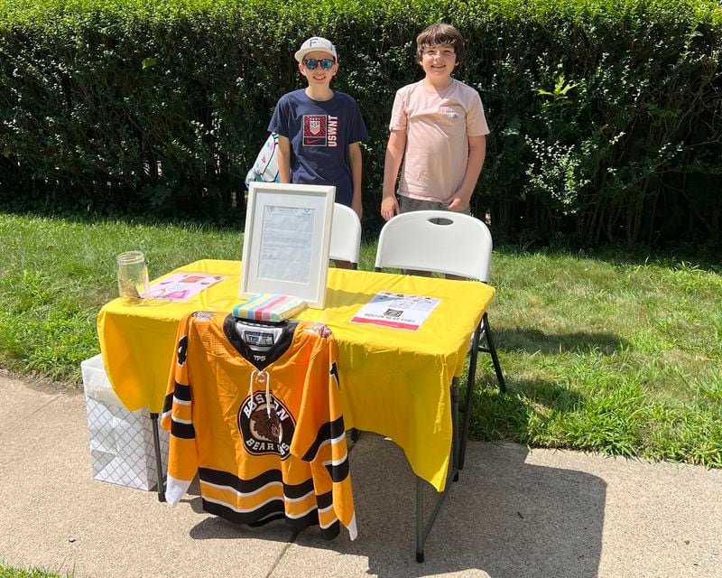 In this Saturday, Aug. 10, 2024 photo provided by Meghan Doherty, Ben Doherty, 12, of Braintree, Mass., left, stands with his cousin Danny Doherty, 12, of Norwood, Mass., right, near a table for donations to the Boston Bear Cubs hockey team, in Norwood. (Meghan Doherty via AP)