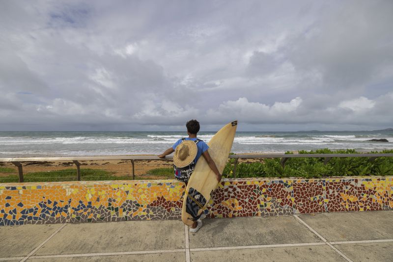 A surfer prepares to enter the water before the passage of Tropical Storm Ernesto at La Pared beach in Luquillo, Puerto Rico, Tuesday, Aug. 13, 2024. (AP Photo/Alejandro Granadillo)