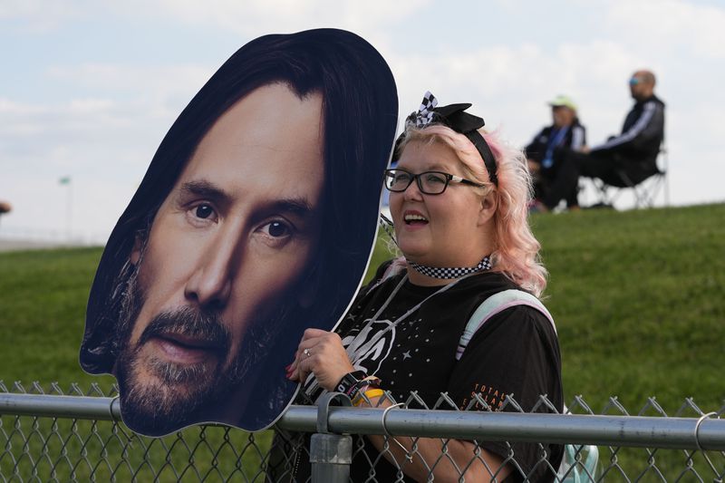 A fan holds a photo of Keanu Reeves as he drives during the GR Cup Series auto race at Indianapolis Motor Speedway, Saturday, Oct. 5, 2024, in Indianapolis. (AP Photo/Darron Cummings)