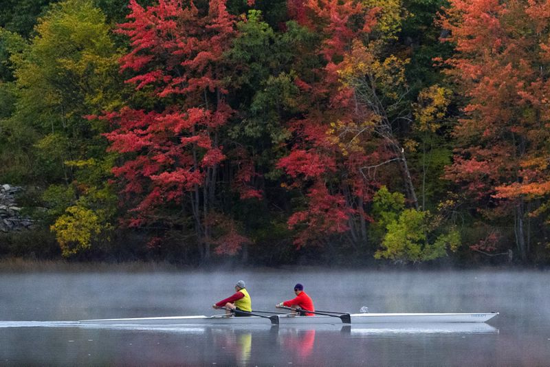 FILE - A pair of rowers glide on the Androscoggin River in Brunswick, Maine, where the foliage has changed to autumn colors, Oct. 10, 2021. (AP Photo/Robert F. Bukaty, File)