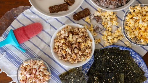 Making snacks with kids is a fun activity for all ages. From left, clockwise: Raspberry-Mango Smoothie Pop, Cherry and Walnut Snack Bars, Sweet and Savory Puppy Chow, cheese-flavored popcorn, Sesame Seaweed Snacks, freeze-dried fruit-flavored popcorn and hot cocoa mix-flavored popcorn (center). (Kate Williams for The Atlanta Journal-Constitution)