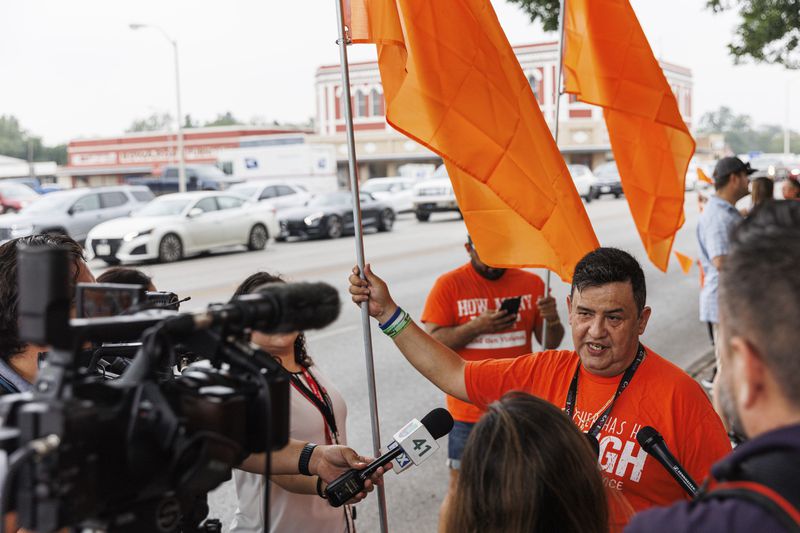Arnulfo "Arnie" Reyes, a survivor of the Robb Elementary mass shooting, talks with reporters as he stands with community members at the town square on Friday morning, May 24, 2024, in Uvalde, Texas. The former Robb Elementary School teacher provided free orange flags signifying gun violence awareness to commemorate the 21 victims – 19 fourth-graders and two teachers – who died two years ago Friday. (Sam Owens/The San Antonio Express-News via AP)