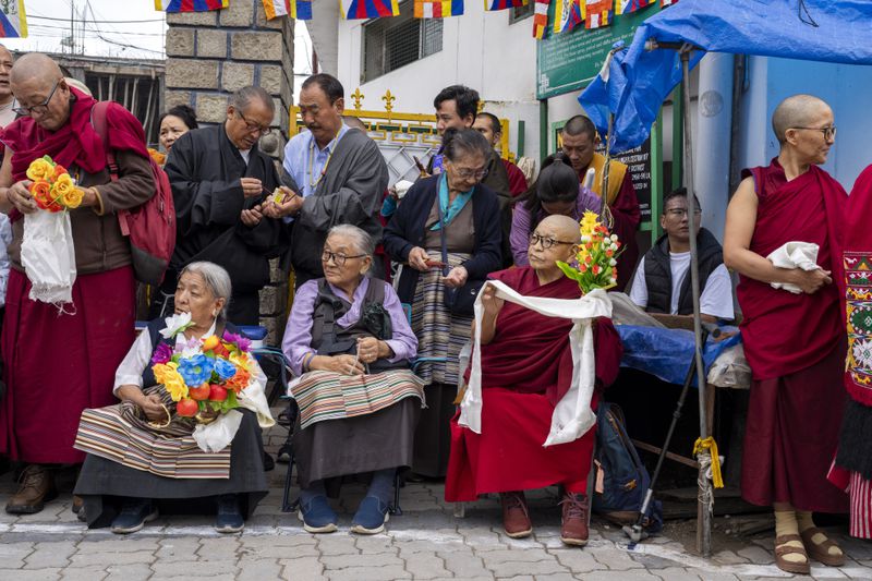 Exiled Tibetans wait with ceremonial scarves and flowers to welcome their spiritual leader the Dalai Lama before he arrives in Dharamshala, India, Wednesday, Aug. 28, 2024. (AP Photo/Ashwini Bhatia)