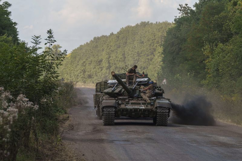 Ukrainian servicemen ride atop a tank, bringing with them a sign reading "Lubimovka" village, after returning from Russia near the Russian-Ukrainian border in Sumy region, Ukraine, Thursday, Aug. 15, 2024. (AP Photo/Evgeniy Maloletka)